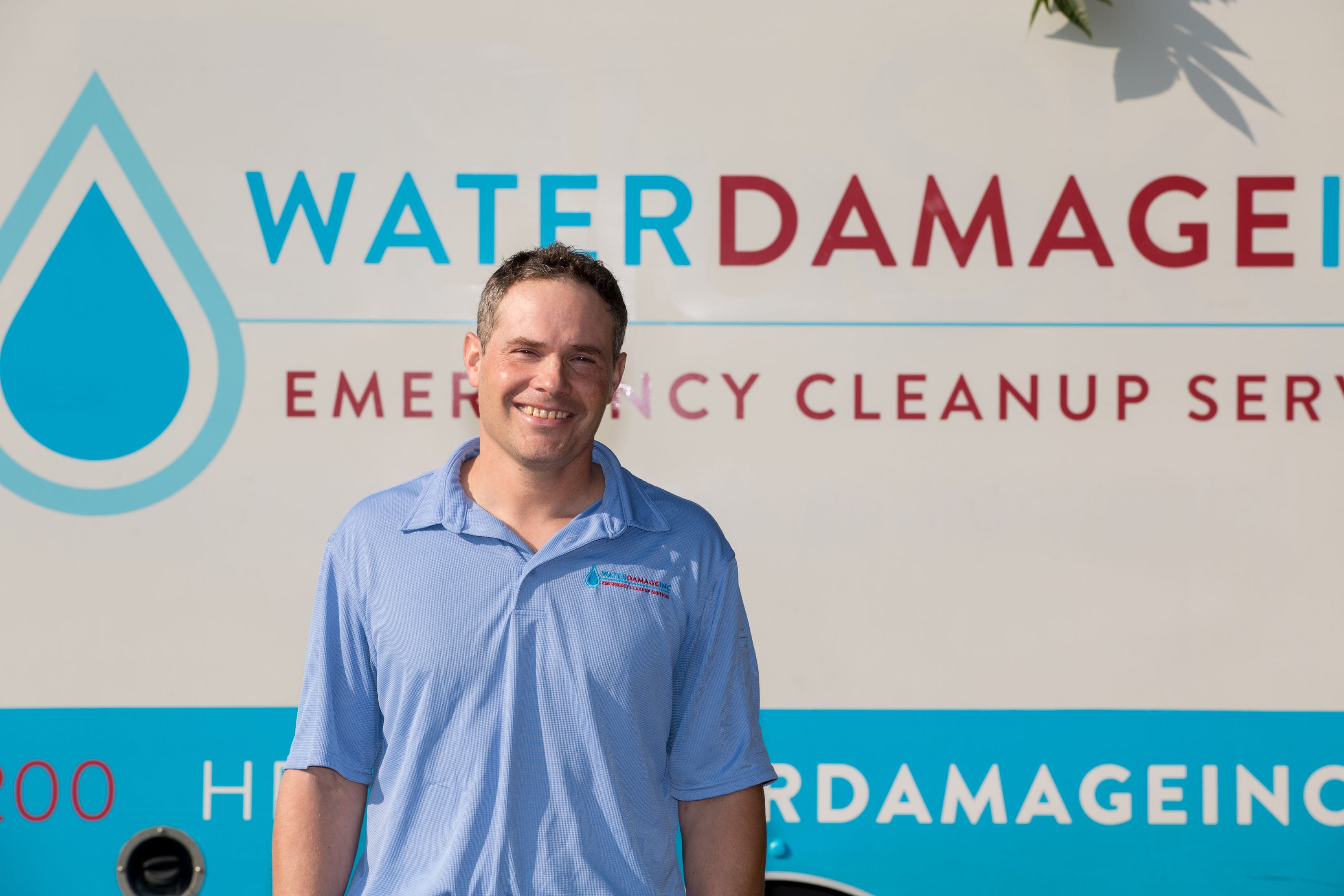A Water Damage Inc. technician in a company polo, standing in front of the company van